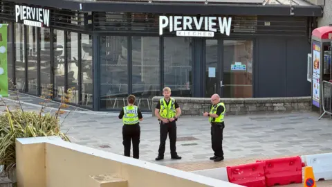 Three police officers in hi-viz vests stand in the middle of an empty pedestrian precinct