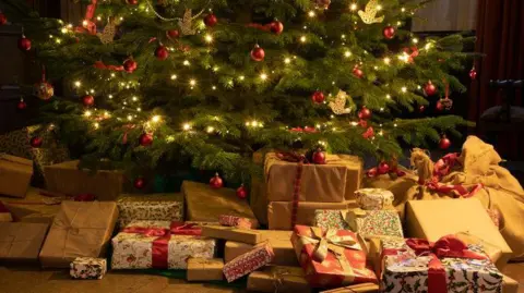 Getty Images A Victorian-style Christmas tree with white lights and red decorations and traditionally-wrapped presents underneath.