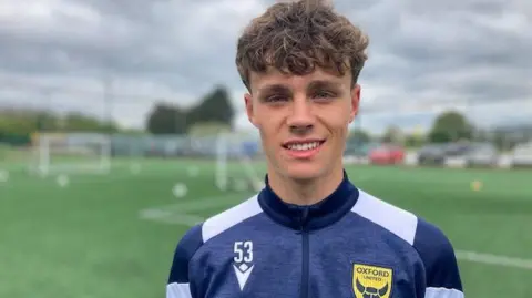 17-year-old Jameson wearing an Oxford United training top in front of a football pitch