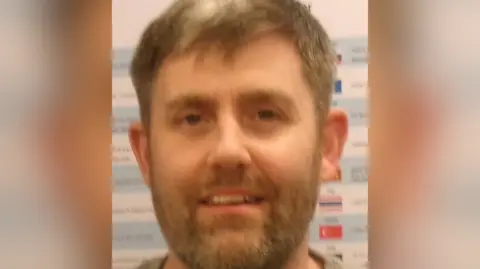 Suffolk Police A headshot of Jamie Sherfield, has a short haircut and facial hair. He is looking directly into the camera. 