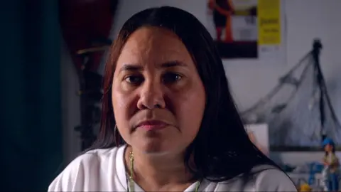 Close up portrait of fishing federation president Yuly Velásquez, she is looking straight at the camera, and is photographed indoors with a fishing net on the wall behind her