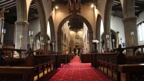 Friends of St Cuthbert's Church The interior of St Cuthbert's Church. There is a royal red carpet and gold gilded furnishings set in a classic church layout.