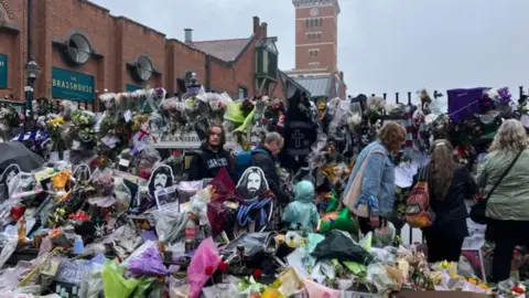 Flowers, pictures and scarves are left draped in the area around the bench on Broad Street.