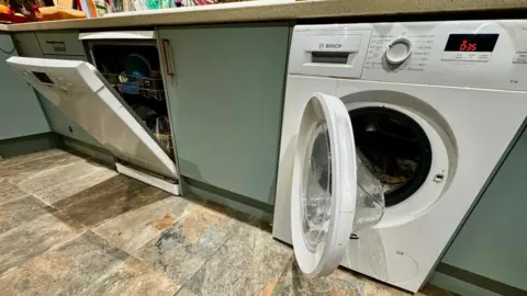 A dishwasher and washing machine left open in a domestic kitchen.