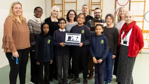 Freia Turland Pupils at May Park Primary and adults involved in the making of the UWE video face the camera in a group shot while holding a laptop showing the animation on 