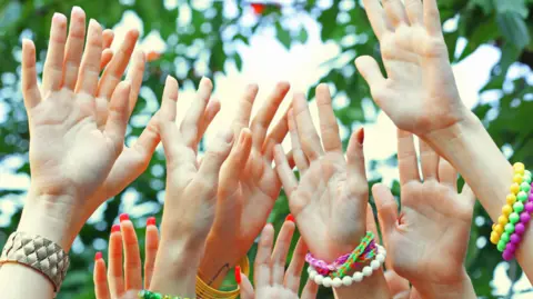 A picture of hands in the air, all wearing colourful bracelets