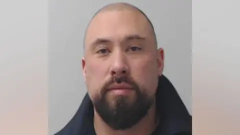 Jonathan Moroney looks at the camera in a police mugshot, he has a beard.