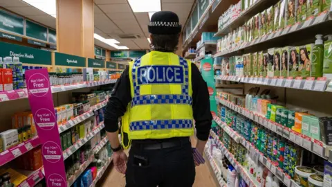 A police officer in high-viz standing in a shop aisle, facing away from the camera