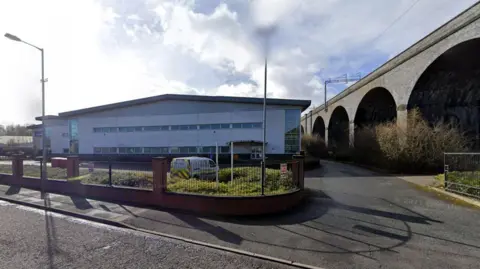 A multi-storey building near a large bridge, as pictured from the adjacent road.
