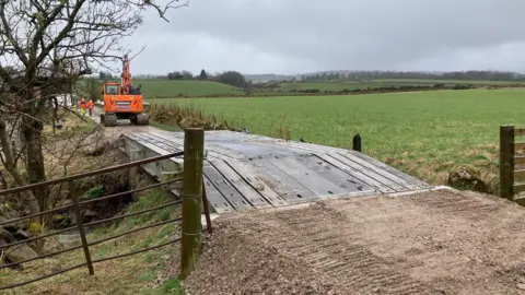 FLS A bridge across a river with a digger at one side and a lot of countryside in the background