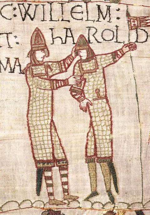 Bayeux Museum A close crop of the same scene, centred on William and Harold embracing, with writing saying 'Willelm' and 'Harold' with fabric texture detail.