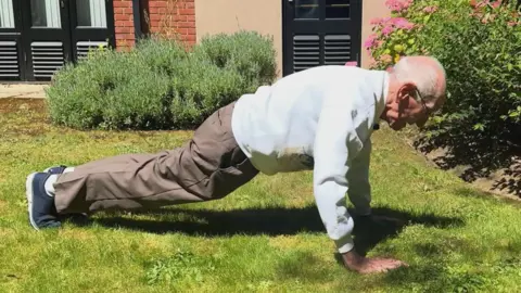George King/BBC An elderly man doing a press-up on grass in a garden.