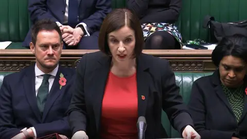 PA Media Education Secretary Bridget Phillipson. She is speaking in the House of Commons. She is wearing a red top under a black blazer. MPs are sitting behind her and beside her on the Commons benches.