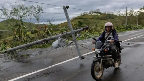 Reuters A man riding a motorcycle past a fallen post, with wires strewn messily around the pole.