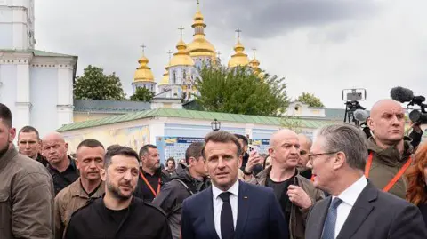 AFP via Getty Images UK Prime Minister Sir Keir Starmer and French President Emmanuel Macron and Volodymyr Zelensky are surrounded by media and army personnel in front of Kyiv's golden domed churches