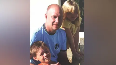 Family handout Michael Mullins is pictured next to his two young children. All three are smiling at the camera. 
