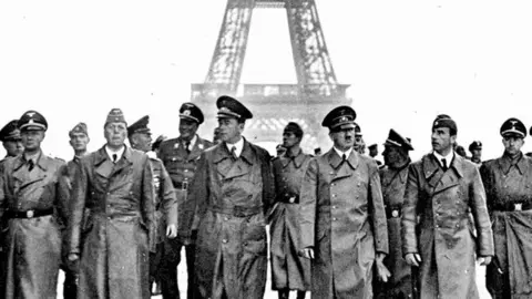 Getty A black and white image of Nazi leader, Adolf Hitler in Paris, on the esplanade of the Chaillot palace, with the architect Albert Speer (on his left), the sculptor Arno Breker (on his right) and his staff. They are all wearing long overcoats and military hats or caps. 