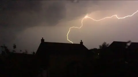 A lightning bolt across the sky above the roofs of houses