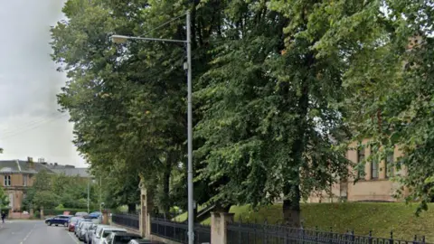 A large lamppost outside a school, with several trees surrounding it