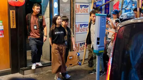 AFP via Getty Images A woman wearing a t-shirt reading "I am a bookstore staffer" being led out of the Have A Nice Stay bookshop by police