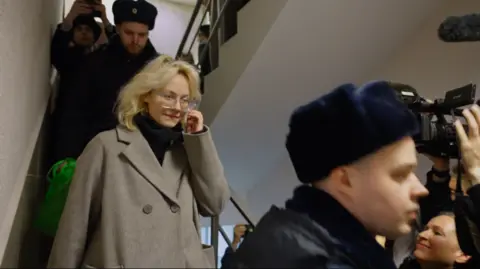 Diana Loginova walks down the stairs, surrounded by police and journalists, in a St Petersburg courthouse