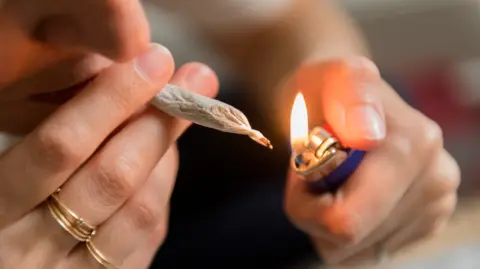 Close up of woman lighting marijuana joint. She's wearing rings on two fingers and also holding a lighter. 