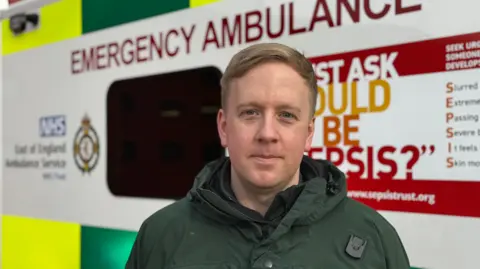 George King/BBC A head and shoulders image of Andrew Benson. He is wearing a green jacket and standing in front of an ambulance. He is looking into the camera.