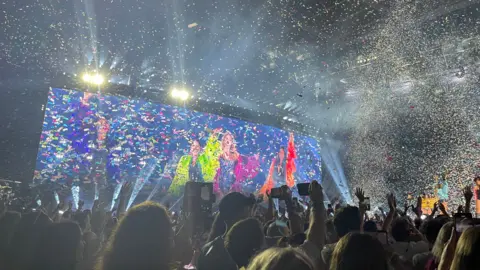 PA Media Taylor Swift performs on stage during her Eras Tour at Wembley Stadium in London. Crowd in the foreground. Confetti falls from the ceiling.