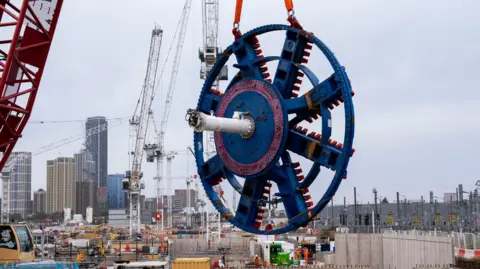 PA Media A red crane lifts a giant blue and red steel 'cutterhead' from one of the Euston Tunnel boring machines at the HS2 site on Atlas Road in Old Oak Common