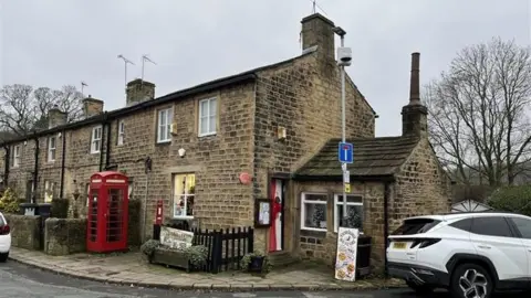 A GV of a stone building in a Yorkshire village with a red post box outside 