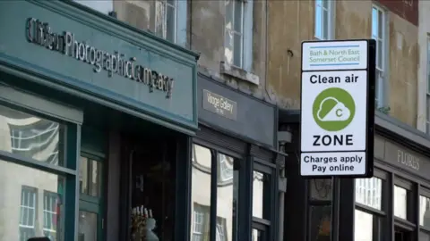 A sign marking the entry to the city of Bath's clean air zone beside shops in the high street. 