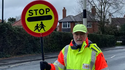 BBC/Oliver Day School crossing patrol officer Bob O'Neill stood with his lollipop at the side of the road