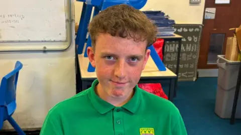 A boy in a green top looks at the camera