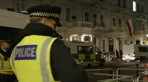 A police officer in a hi vis jacket is seen stood outside the Iranian embassy 