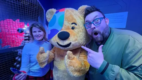 Pudsey (middle), Adam Ball (right), Sophie Aldred (left) in a Dr Who themed escape room