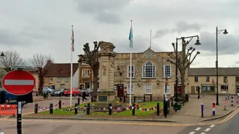 Google War memorial set in a grass square with flags in front of the town hall