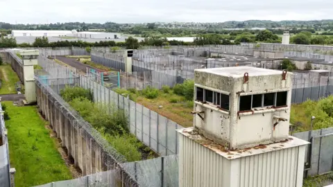 PA Media A dilapidated guard house and several fences at the former Maze prison site which is overgrown with vegetation