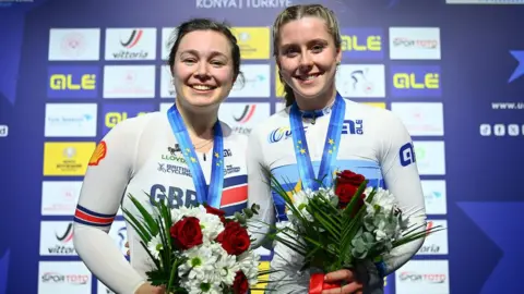 Sophie Capewell and Emma Finucane smiling with medals around the necks and holding flowers