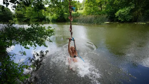 A woman on a rope swing in the river Avon at Warleigh Weir in Bath. She is making a splash as she enters the water