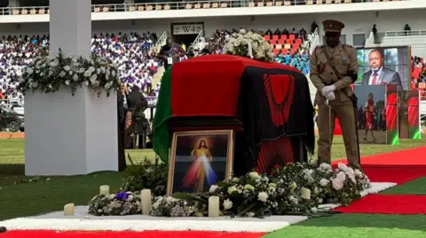 Malawi State House A coffin draped with Malawi's flag with a guard of honour looking on