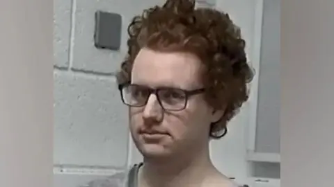 Thames Valley Police Gwyn Samuels looks at the camera, wearing dark glasses. They have dark short curly hair.