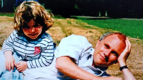 Charlie Ward Charlie and her dad Steven are laying on grass in a field. The photo is from her childhood