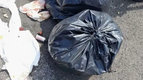 Wiltshire Council Black bags left in a layby in Salisbury. Rubbish is strewn across the floor.