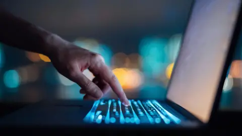 Close up of woman's hand typing on computer keyboard in the dark against colourful bokeh in background, working late on laptop at home - stock photo