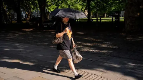 A woman walking through Queen's Square in Bristol is holding a parasol