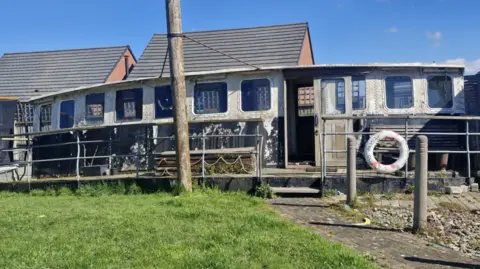 A structure with a roof on a boat that provides shelter for the person who is controlling the direction of the boat. The wheelhouse is situated at the back of a garden. 