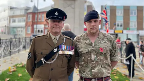 Two men in military uniform stand in front of the cenotaph on Regent's Parade in Swindon