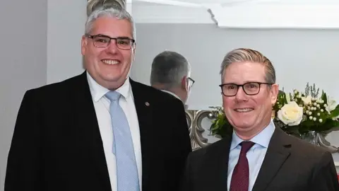 PA Media Two men in formal attire smiling for a picture in front of a mirror.