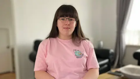 Woman with long brown hair wear a pink t-shirt sitting in a living room