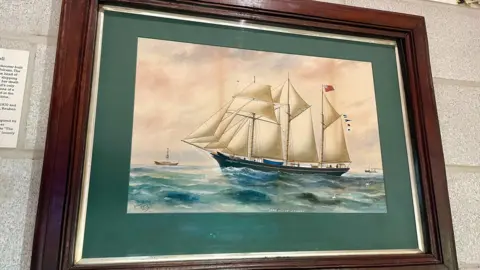 Cornwall Council A painting in a wooden frame showing a boat at sea with white sails.